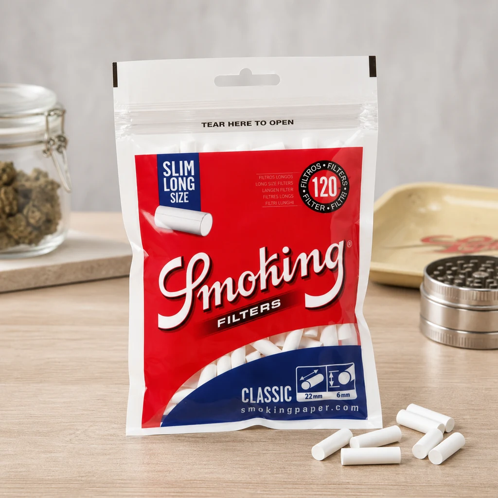 Bolsa roja y azul de filtros Smoking Slim Long con varios filtros blancos sueltos sobre una mesa y un grinder al fondo.