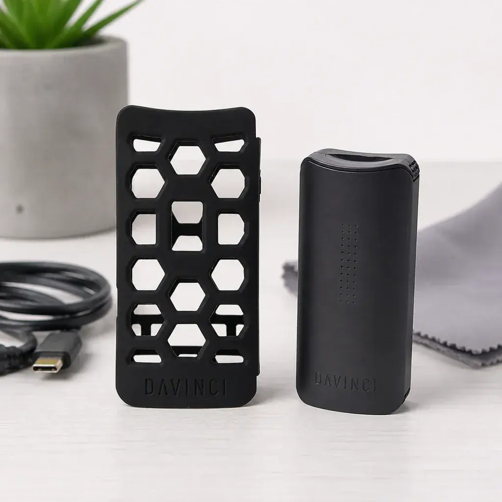 Funda negra DaVinci Miqro C con aberturas geométricas junto a un vaporizador negro, con cable y paño sobre la mesa.