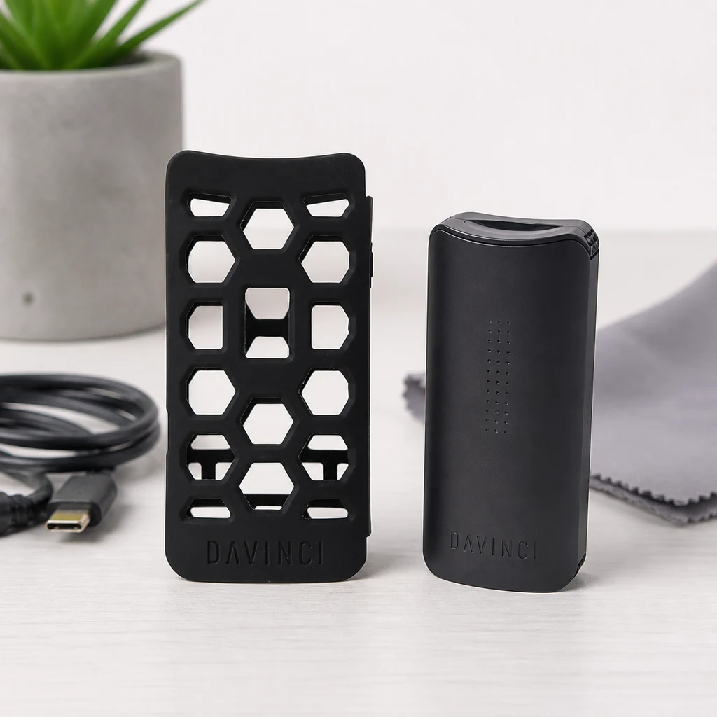 Funda negra DaVinci Miqro C con aberturas geométricas junto a un vaporizador negro, con cable y paño sobre la mesa.