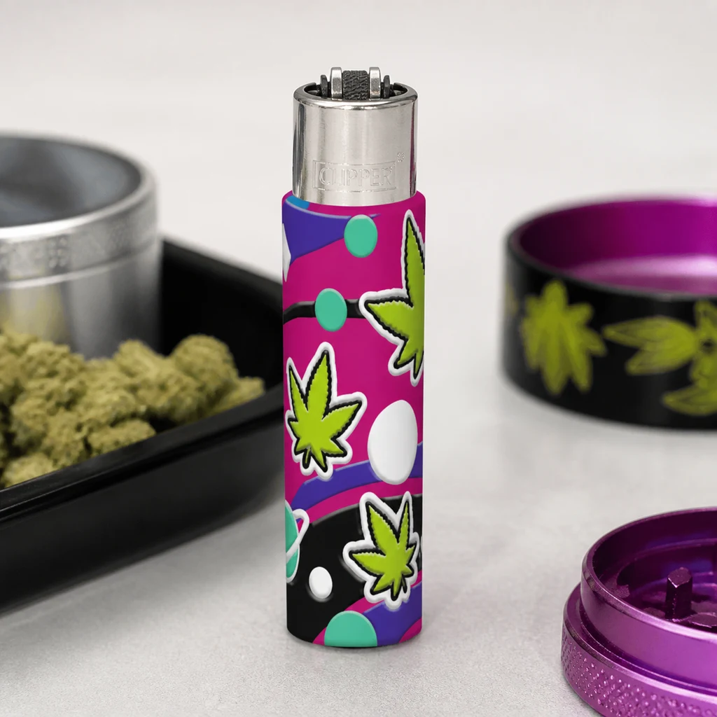 Encendedor Clipper con funda de motivos pop art y hojas verdes, de pie junto a un grinder morado abierto y una bandeja con cogollos.