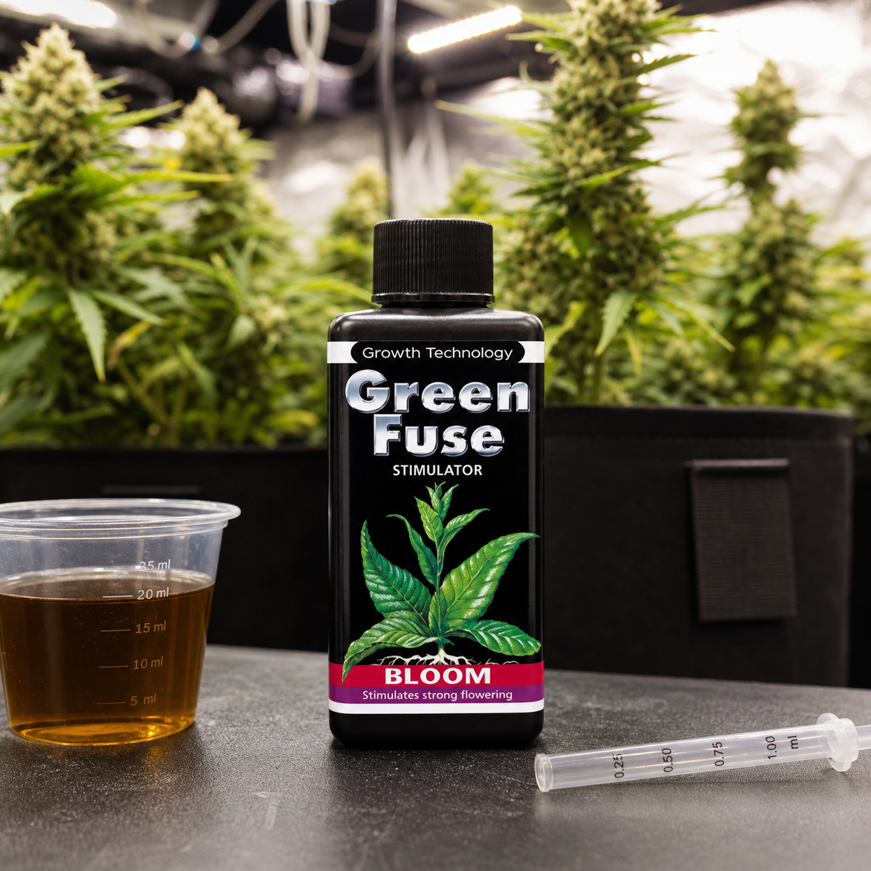 Botella negra Green Fuse Bloom junto a un vaso graduado con líquido ámbar y una jeringa dosificadora, con plantas en floración al fondo.