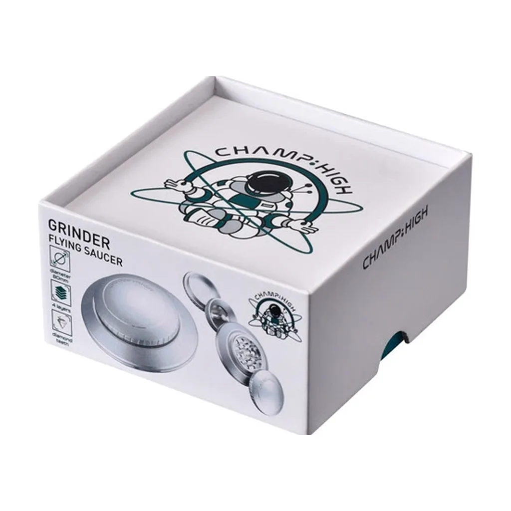 Caja blanca del grinder Champ High Flying Saucer, con un astronauta en la tapa y vistas del grinder cerrado y desmontado en el frontal.