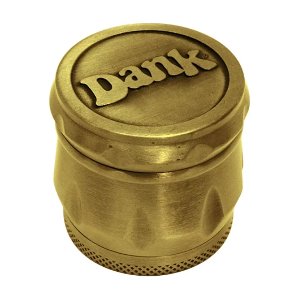 Grinder Dank de acabado dorado, con nombre en relieve en la tapa, hendiduras laterales y borde inferior texturizado, sobre fondo blanco.