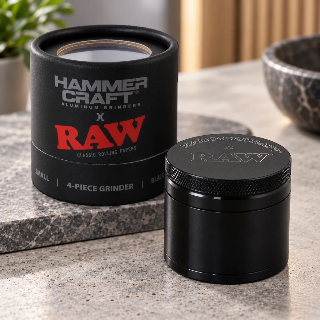 Grinder negro cerrado con borde estriado y logotipo Hammercraft x RAW en la tapa, junto a su caja cilíndrica negra.
