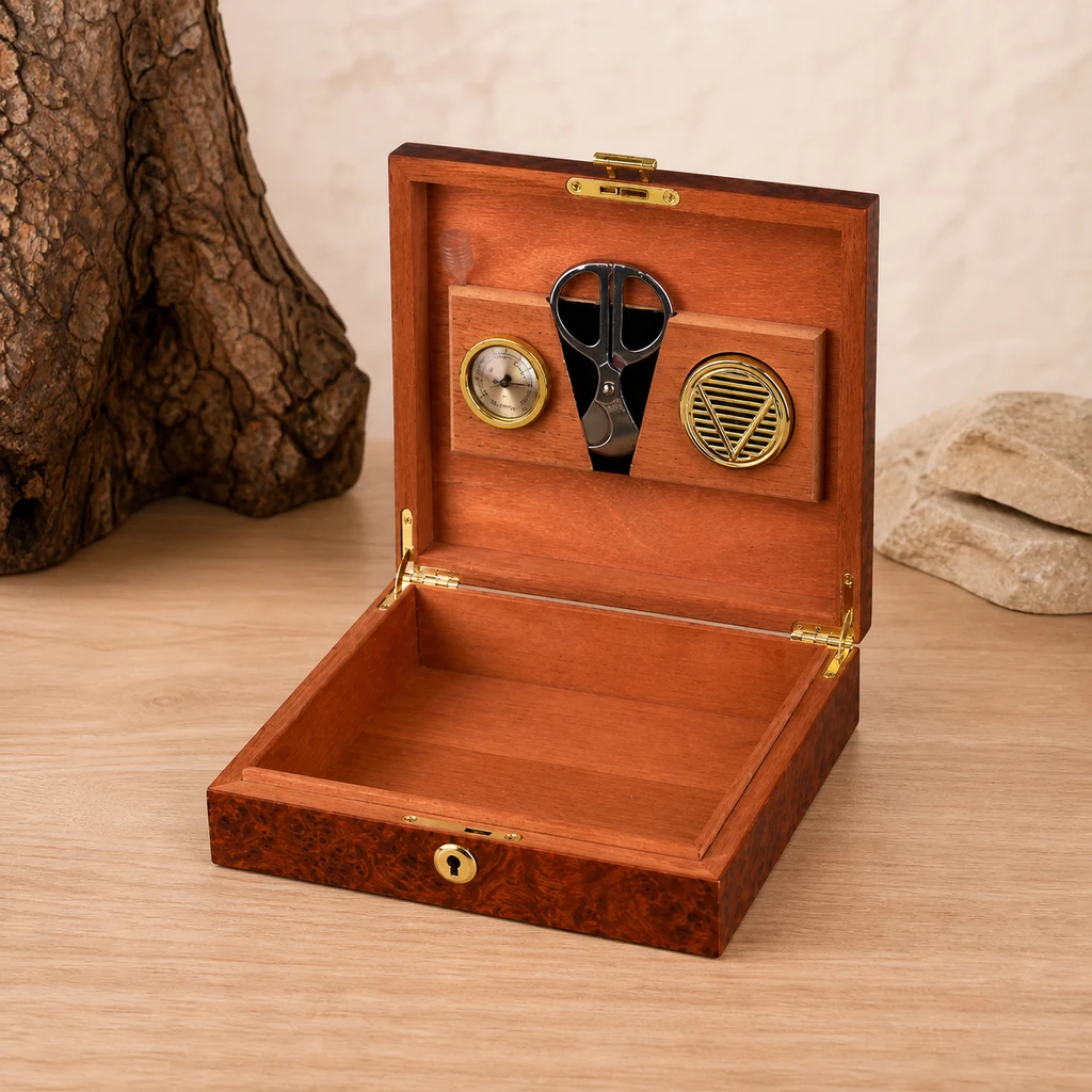Humidor de madera abierto sobre una mesa, con interior vacío, higrómetro, humidificador circular y tijeras sujetos a la tapa. Humidor de madera abierto sobre una mesa, con interior vacío, higrómetro, humidificador circular y tijeras sujetos a la tapa.