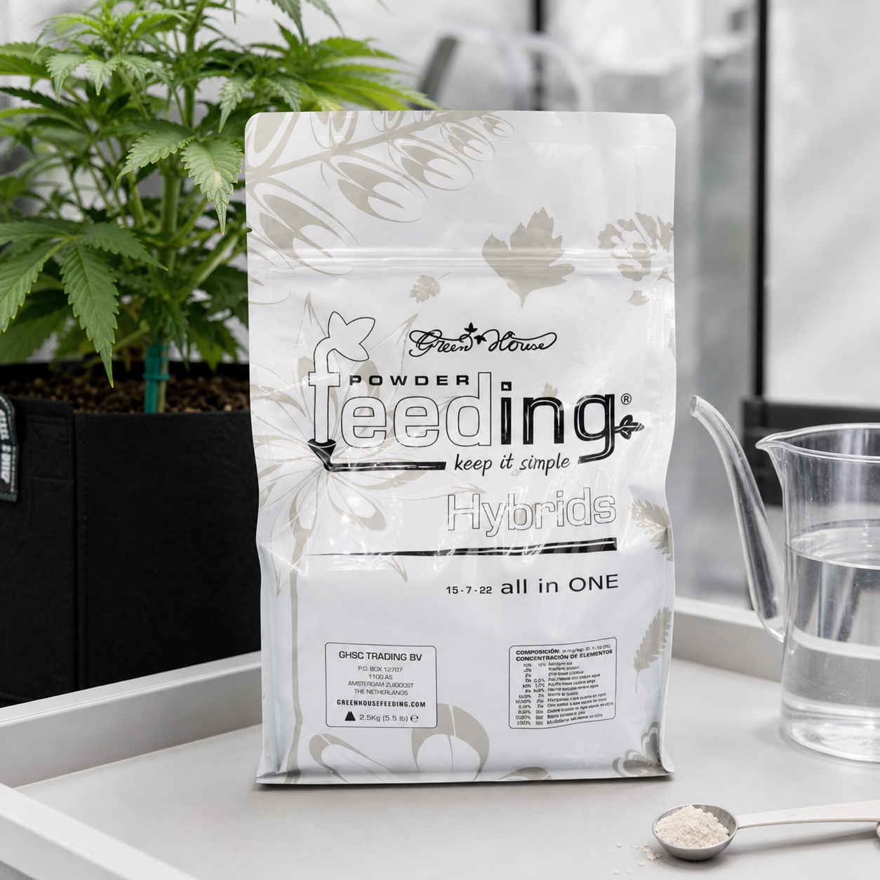 Bolsa de Powder Feeding Hybrids con la indicación 15-7-22, junto a una planta, una jarra con agua y una cuchara con polvo.