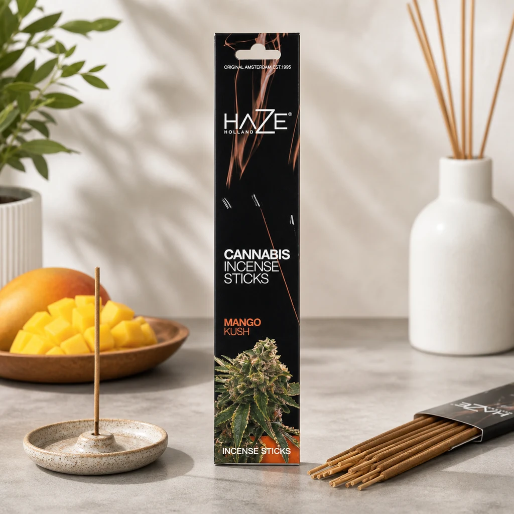 Caja de incienso Haze Mango Kush con varillas sobre una mesa, una colocada en un soporte cerámico, junto a mango y un jarrón.