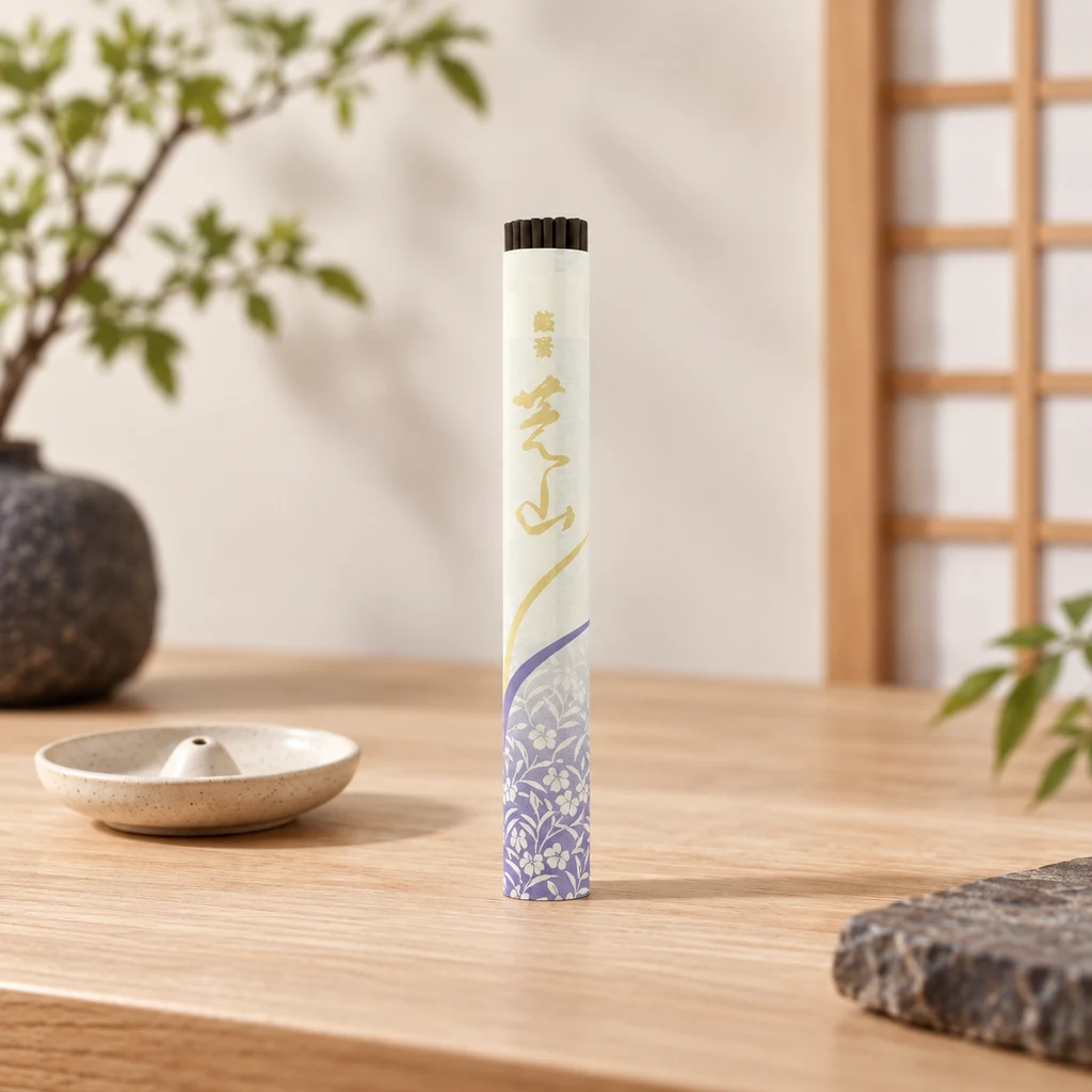 Envase alargado de incienso Meiko Shibayama con motivos florales violetas y letras doradas, sobre una mesa junto a un portaincienso. Envase alargado de incienso Meiko Shibayama con motivos florales violetas y letras doradas, sobre una mesa junto a un portaincienso.