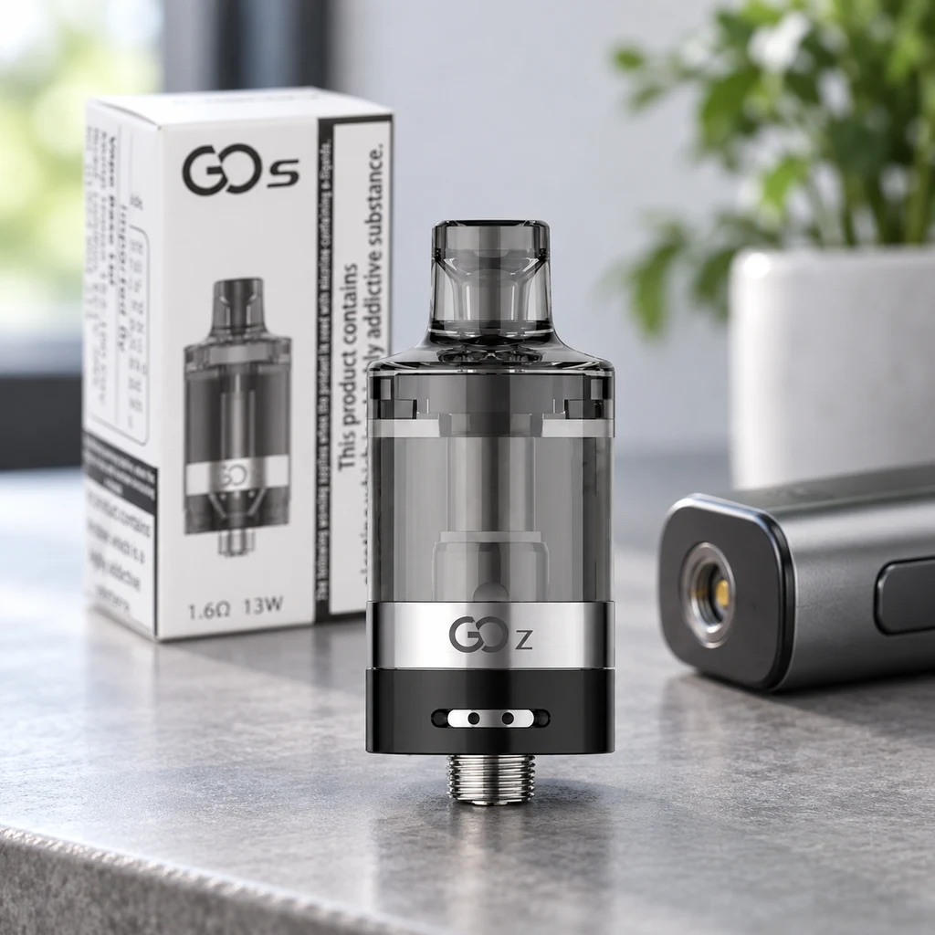 Atomizador de depósito transparente oscuro, base negra y aro plateado marcado «GO Z», junto a una caja «GO S» y un dispositivo de vapeo.