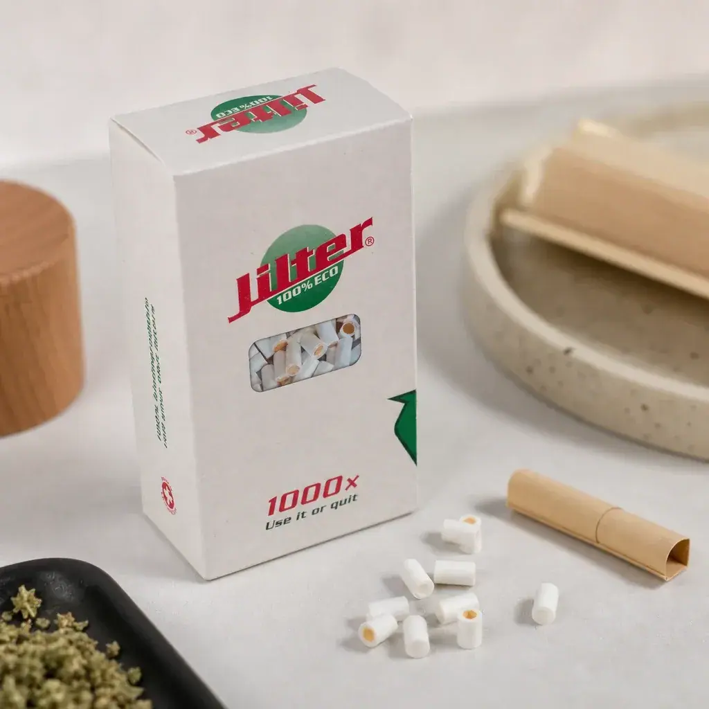 Caja de filtros Jilter con ventana frontal, varios filtros blancos sobre la mesa y papel de liar marrón a su lado.
