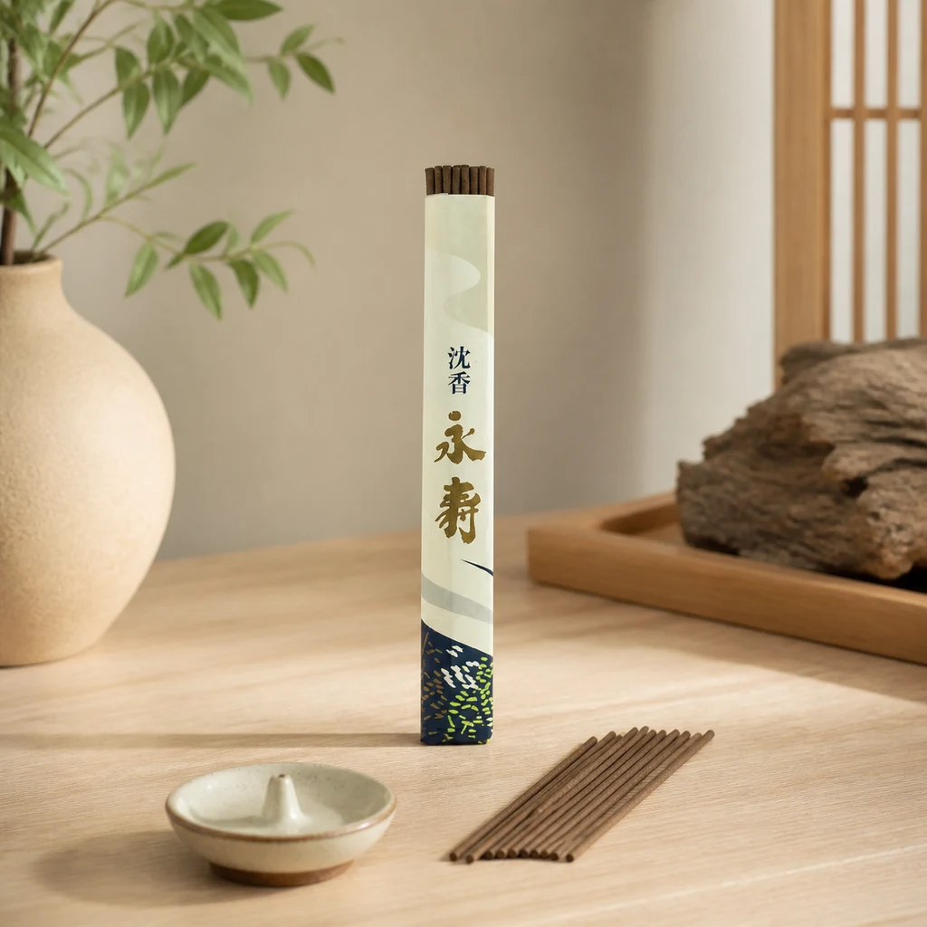 Envase de incienso Jinkoh Eiju con caracteres japoneses, varillas marrones y un pequeño soporte sobre una mesa junto a un jarrón.
