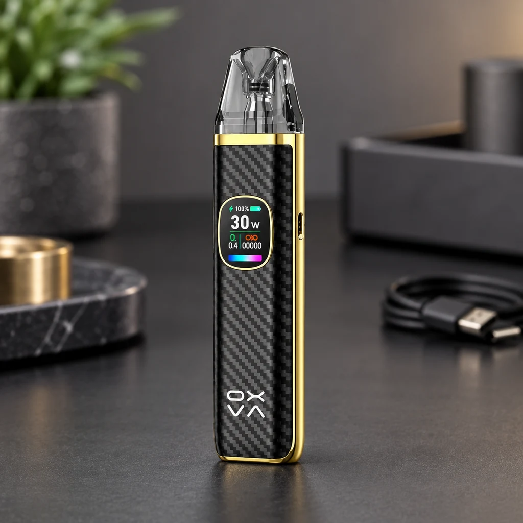 Vaper Oxva negro con patrón diagonal, bordes dorados y boquilla transparente; pantalla con 30 W, sobre una mesa junto a un cable USB.