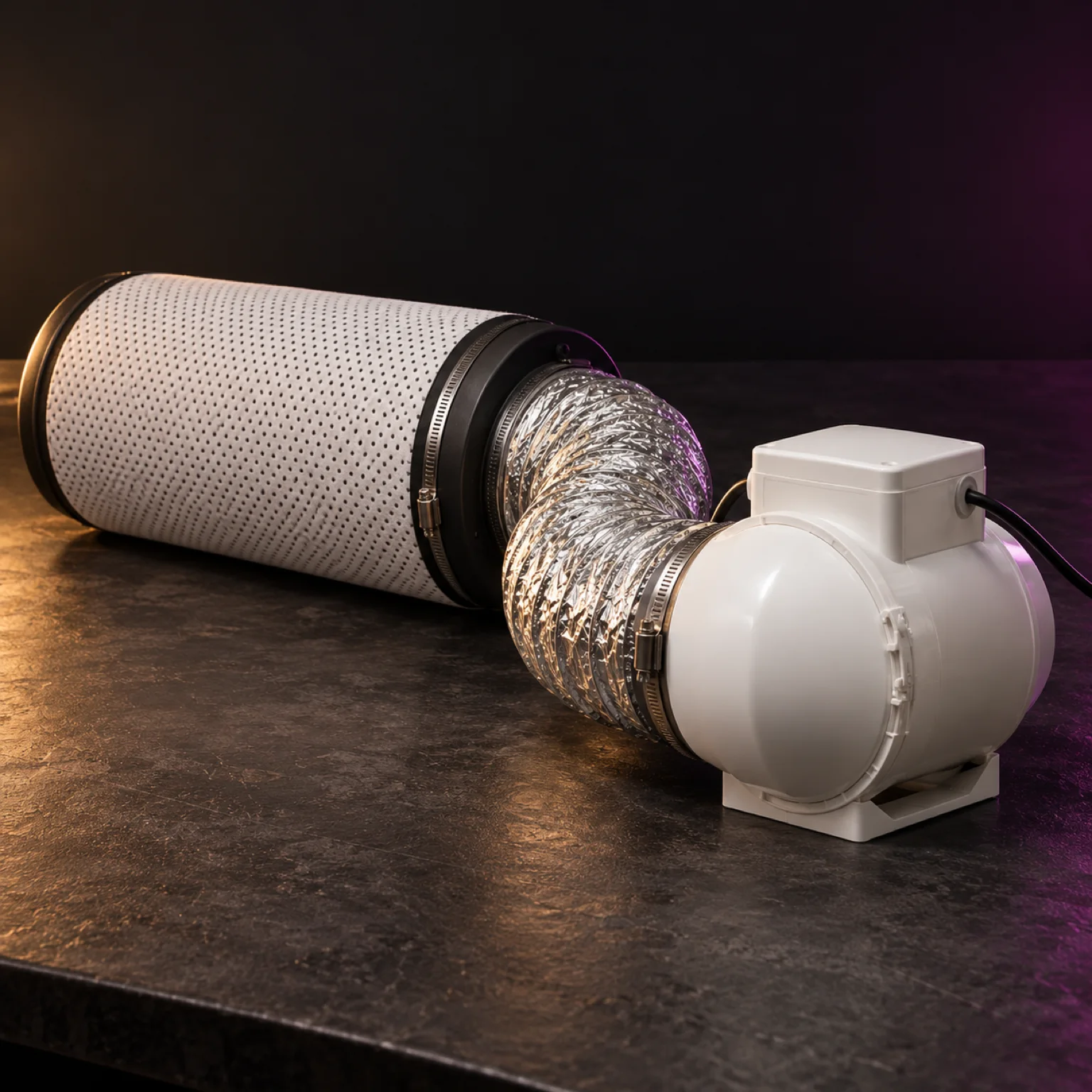 Kit de ventilación con filtro de carbón cilíndrico conectado mediante un conducto flexible plateado a un extractor blanco sobre una mesa oscura.