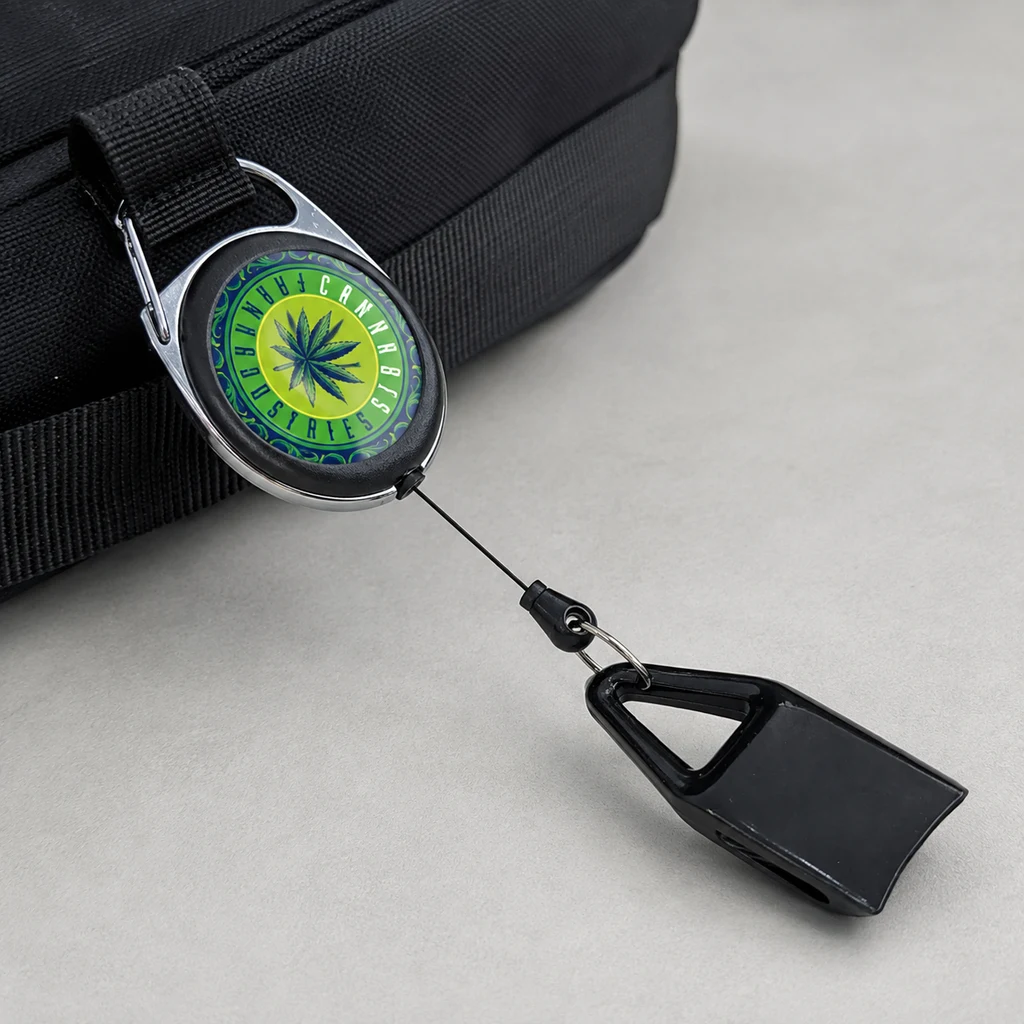 Llavero portamecheros sujeto a una bolsa negra, con emblema de hoja de cannabis y cable extendido hasta un soporte negro vacío.