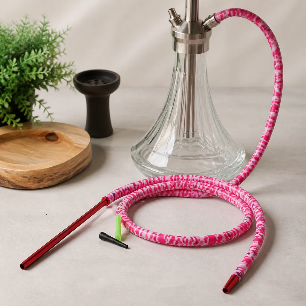 Manguera rosa y blanca enrollada junto a una cachimba de base transparente, con boquilla roja alargada y pequeños accesorios.