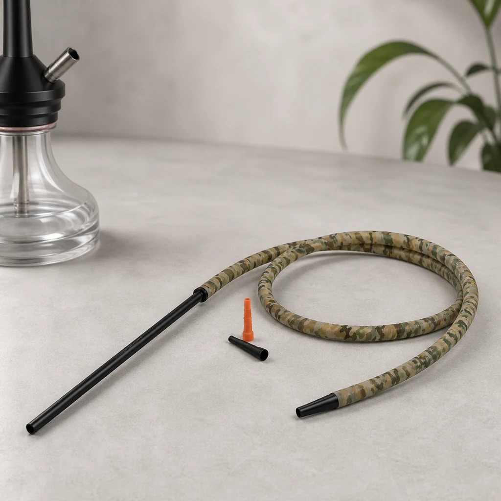 Manguera de cachimba con estampado de camuflaje enrollada, boquilla negra larga y dos adaptadores sueltos junto a una cachimba.