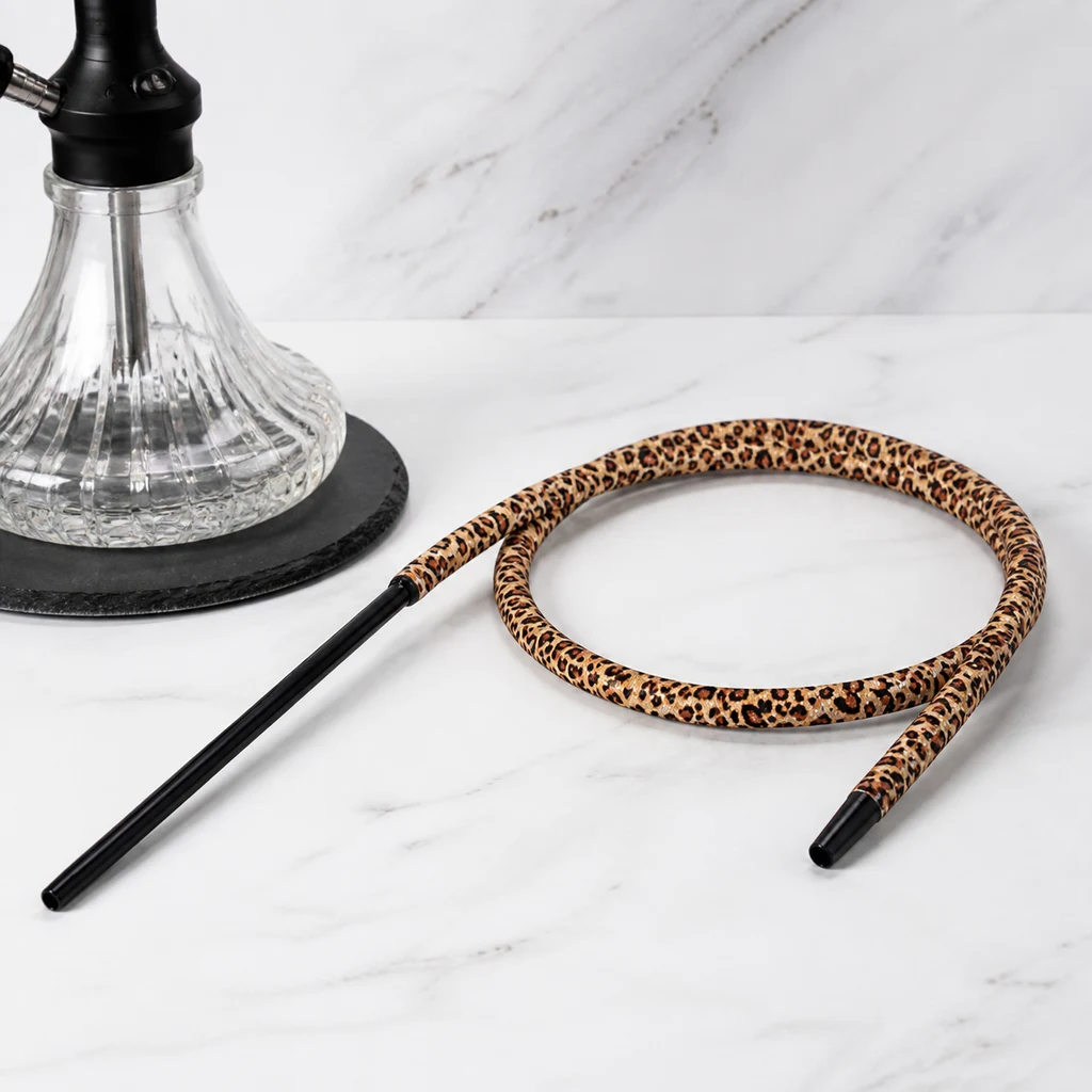 Manguera de cachimba con estampado de leopardo, enrollada y con boquilla negra, junto a una base transparente sobre superficie blanca.