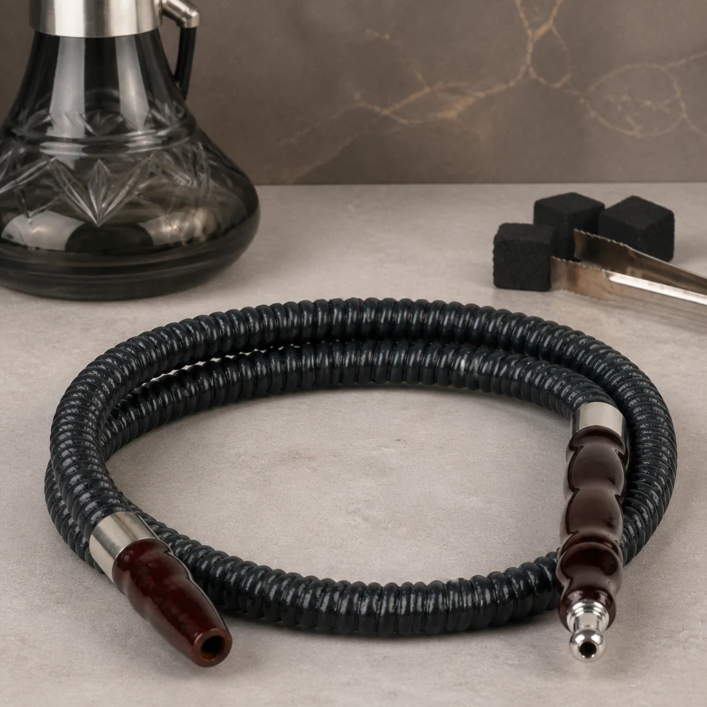 Manguera negra de cachimba enrollada, con extremos marrones y conexiones plateadas, junto a una base de cachimba, carbones y pinzas. Manguera negra de cachimba enrollada, con extremos marrones y conexiones plateadas, junto a una base de cachimba, carbones y pinzas.
