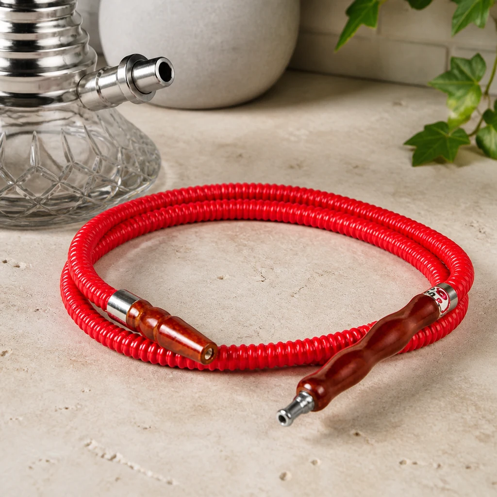 Manguera roja de cachimba enrollada, con extremos marrones y conexiones metálicas, junto a una base de cristal. Manguera roja de cachimba enrollada, con extremos marrones y conexiones metálicas, junto a una base de cristal.