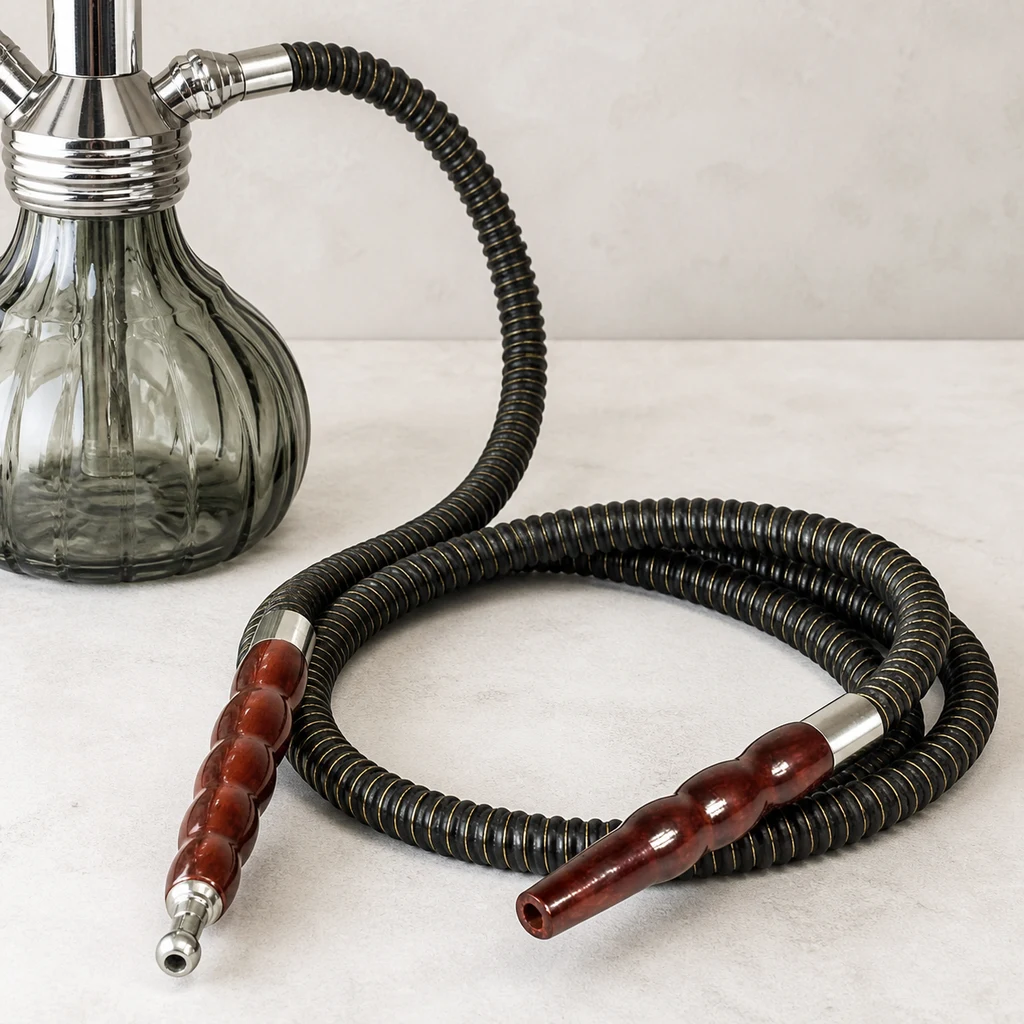 Manguera negra de cachimba enrollada, con extremos marrones y conexiones plateadas, junto a una base de vidrio acanalado. Manguera negra de cachimba enrollada, con extremos marrones y conexiones plateadas, junto a una base de vidrio acanalado.
