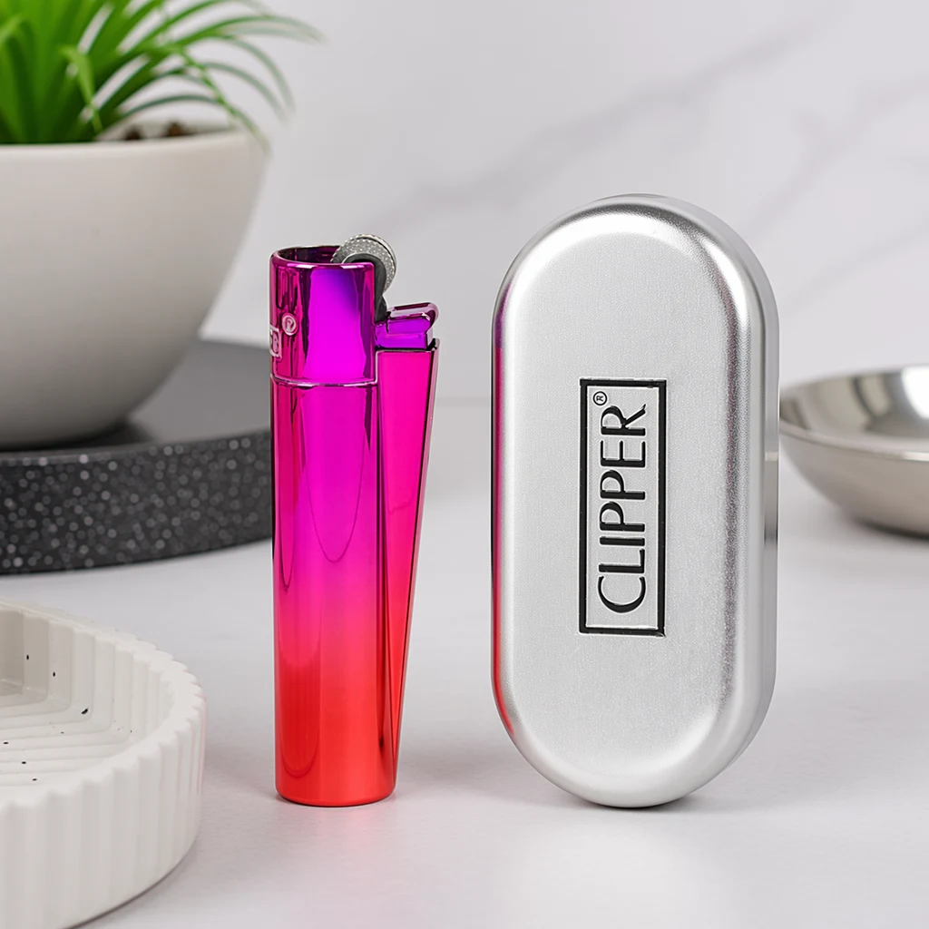 Encendedor Clipper con acabado brillante en degradado fucsia y rojo, junto a un estuche plateado con el logotipo de la marca.