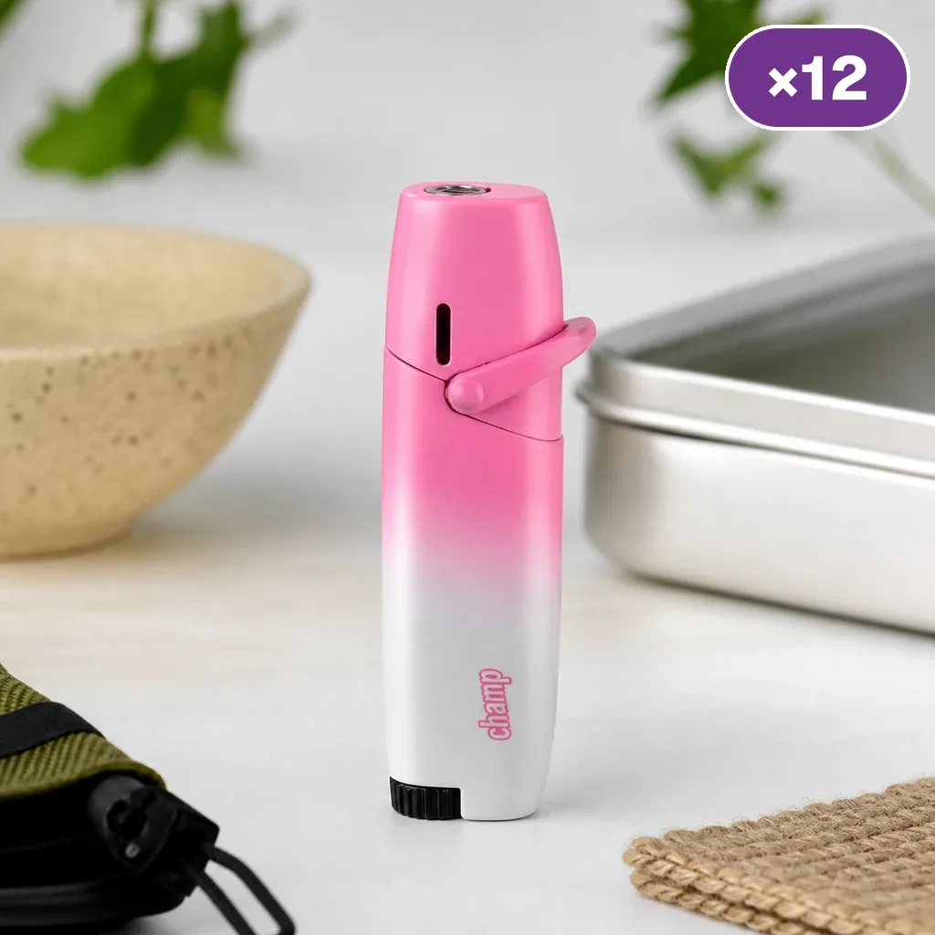 Encendedor Champ con degradado rosa y blanco, palanca lateral y base negra sobre una mesa; distintivo superior con la cifra 12.