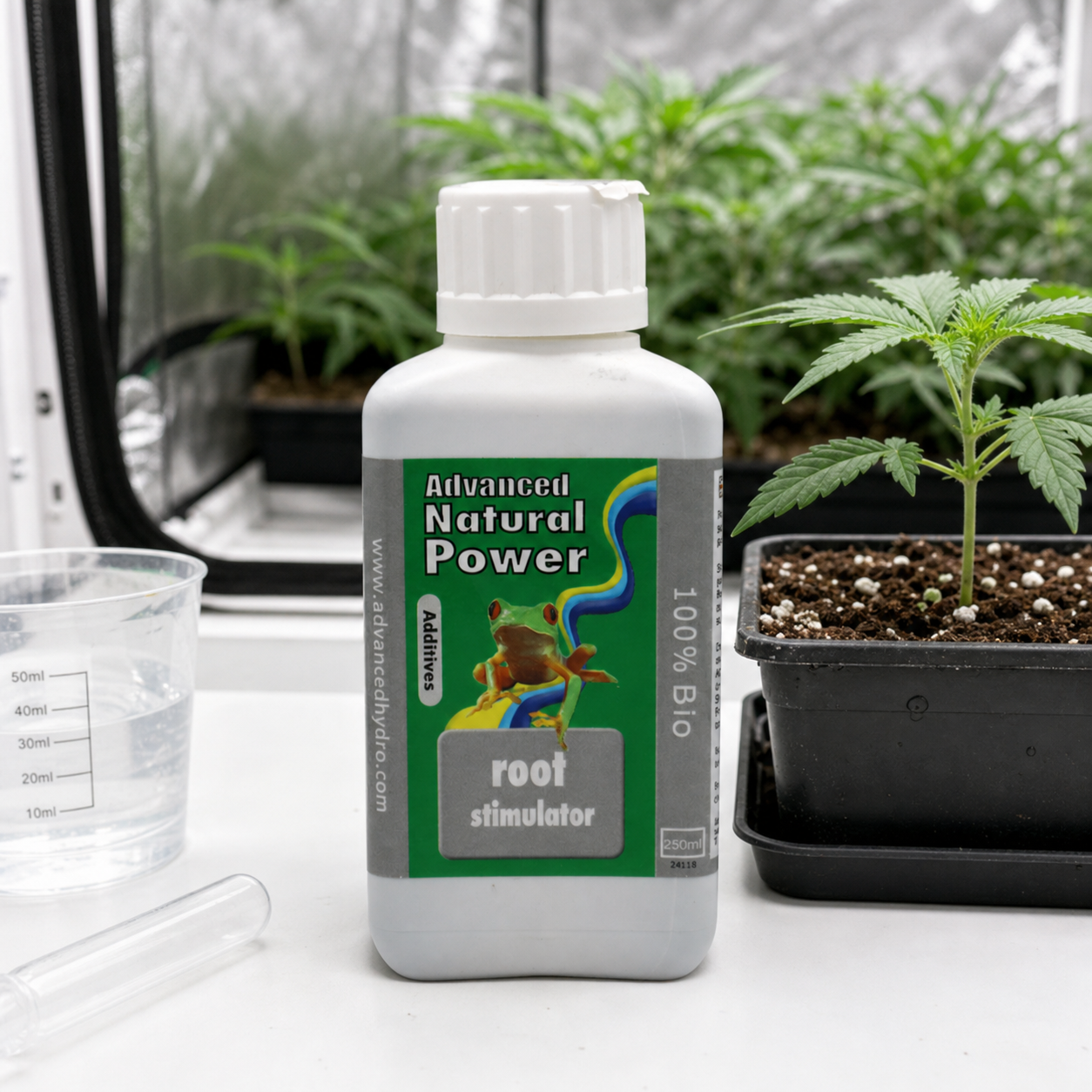 Bote de Advanced Natural Power Root Stimulator con etiqueta verde y una rana, junto a una maceta, un vaso graduado y una pipeta.