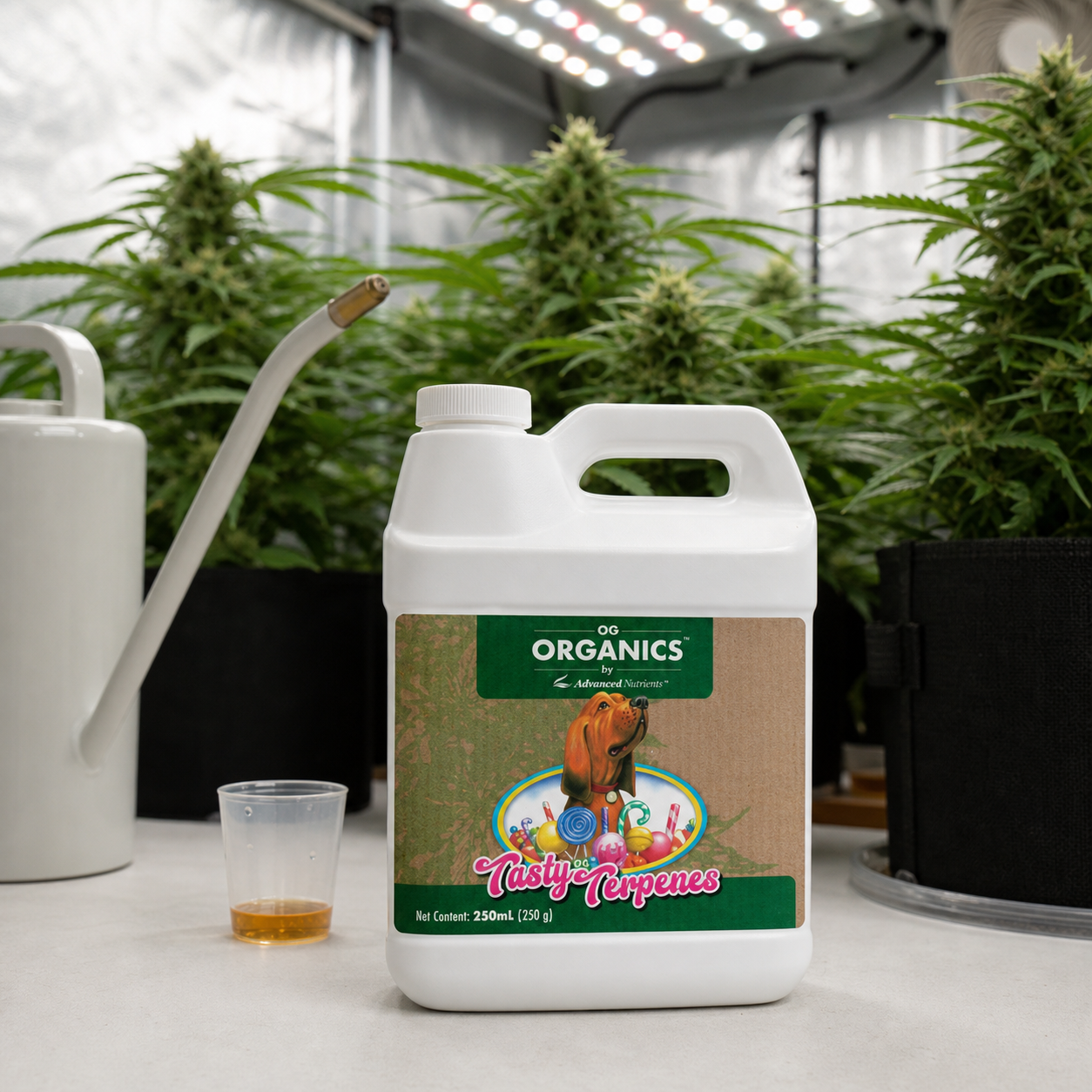 Garrafa blanca de OG Organics Tasty Terpenes junto a un vaso dosificador y una regadera, con plantas bajo luces de cultivo al fondo.