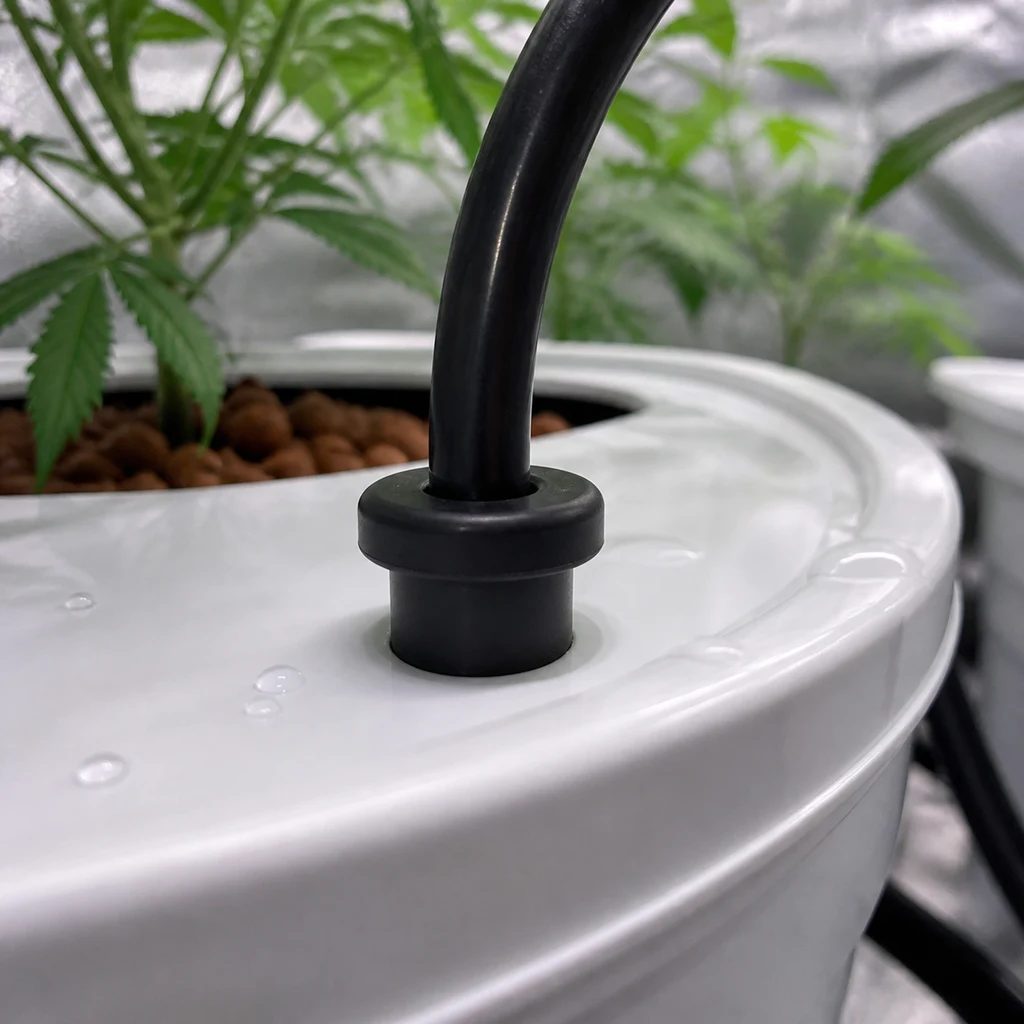 Detalle de un ojal negro Top Hat GHE alrededor de un tubo que atraviesa la tapa blanca de un recipiente, con plantas al fondo.