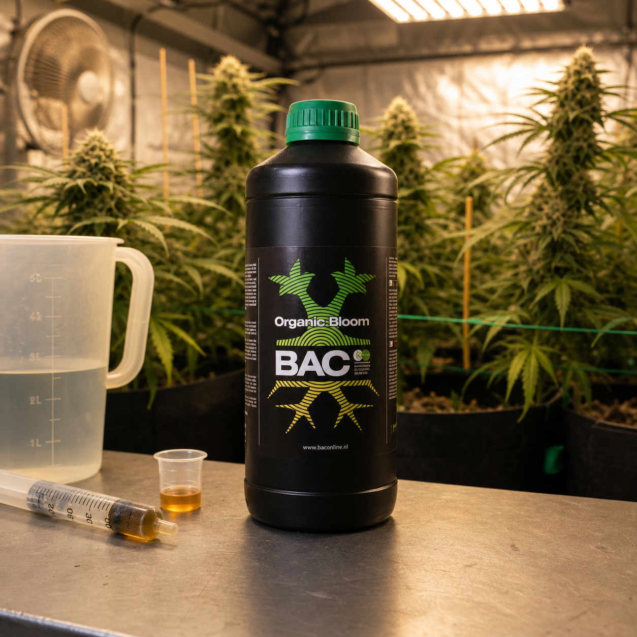 Botella negra de BAC Organic Bloom con tapón verde, junto a una jarra medidora, una jeringa y un vasito, ante plantas en floración.