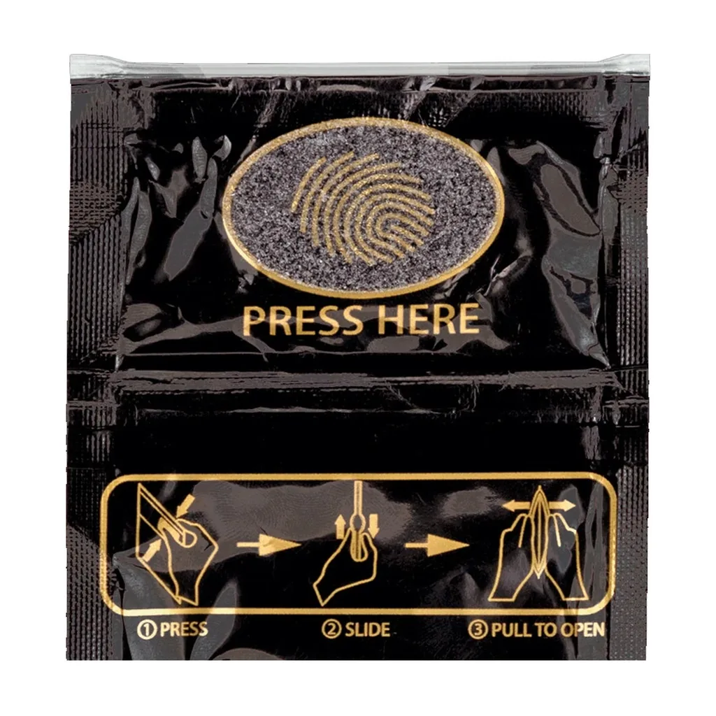 Bolsa negra con una huella dorada, texto «Press Here» e instrucciones ilustradas para presionar, deslizar y tirar para abrir. Bolsa negra con una huella dorada, texto «Press Here» e instrucciones ilustradas para presionar, deslizar y tirar para abrir.