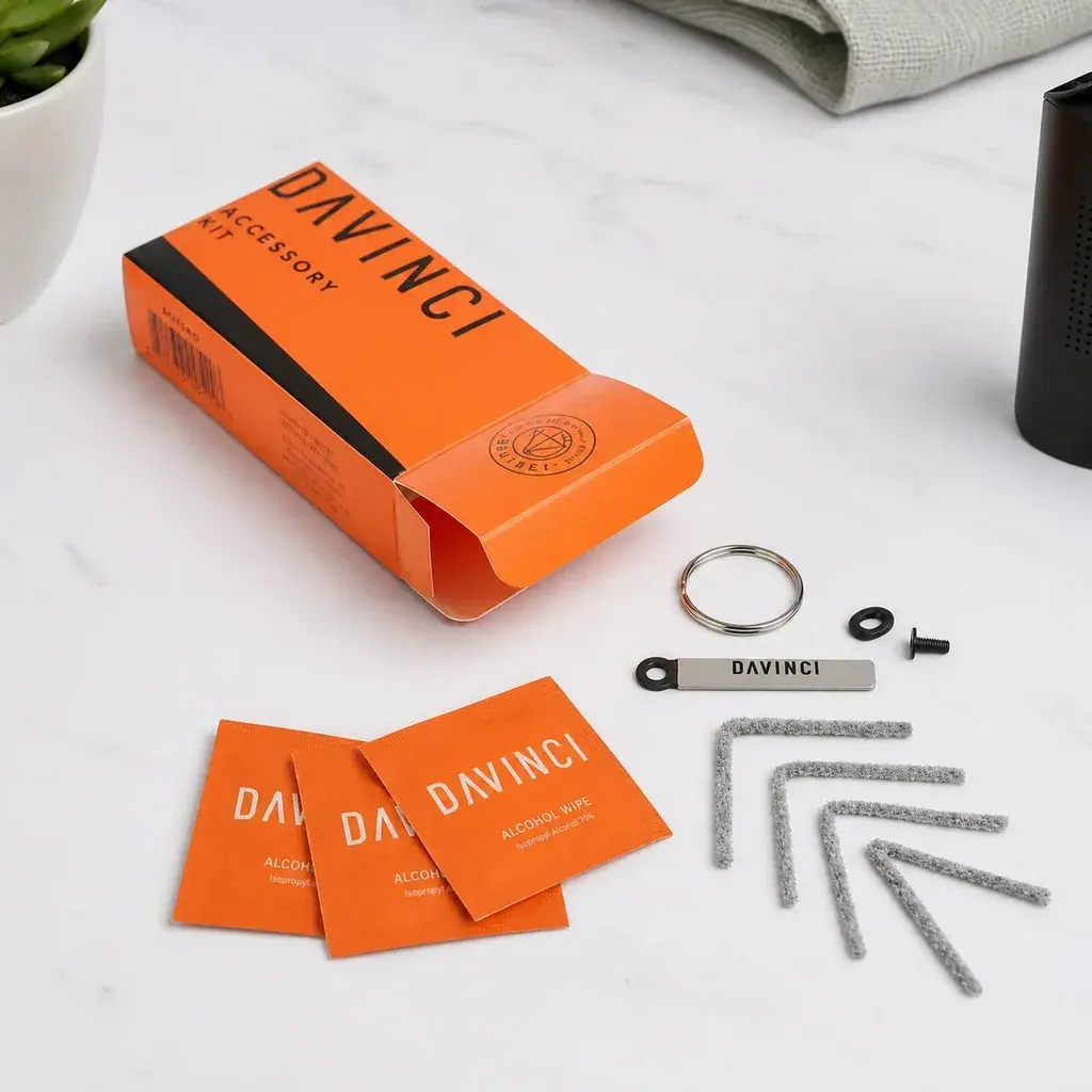 Kit de accesorios DaVinci con caja naranja abierta, sobres de toallitas, limpiadores angulares, una anilla y pequeñas piezas de repuesto.