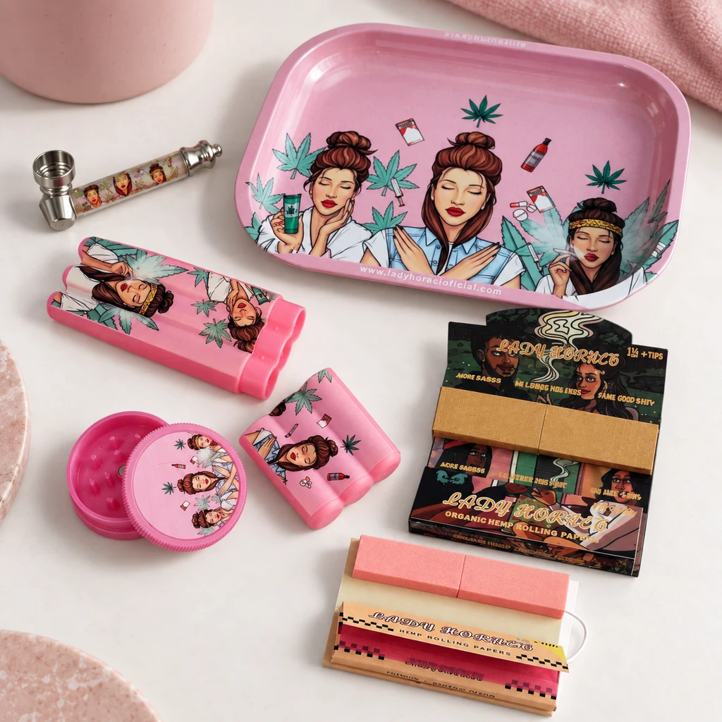 Bandeja rosa y accesorios para fumar sobre una mesa, con pipa, triturador y papeles, decorados con mujeres y hojas de cannabis.