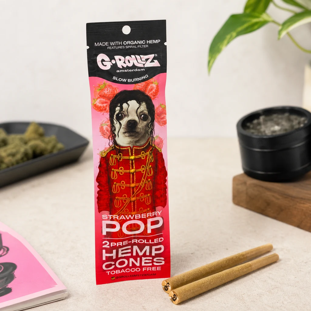 Envase rosa G-Rollz Strawberry Pop con un perro ilustrado y dos conos marrones delante; al fondo, una bandeja y un grinder.