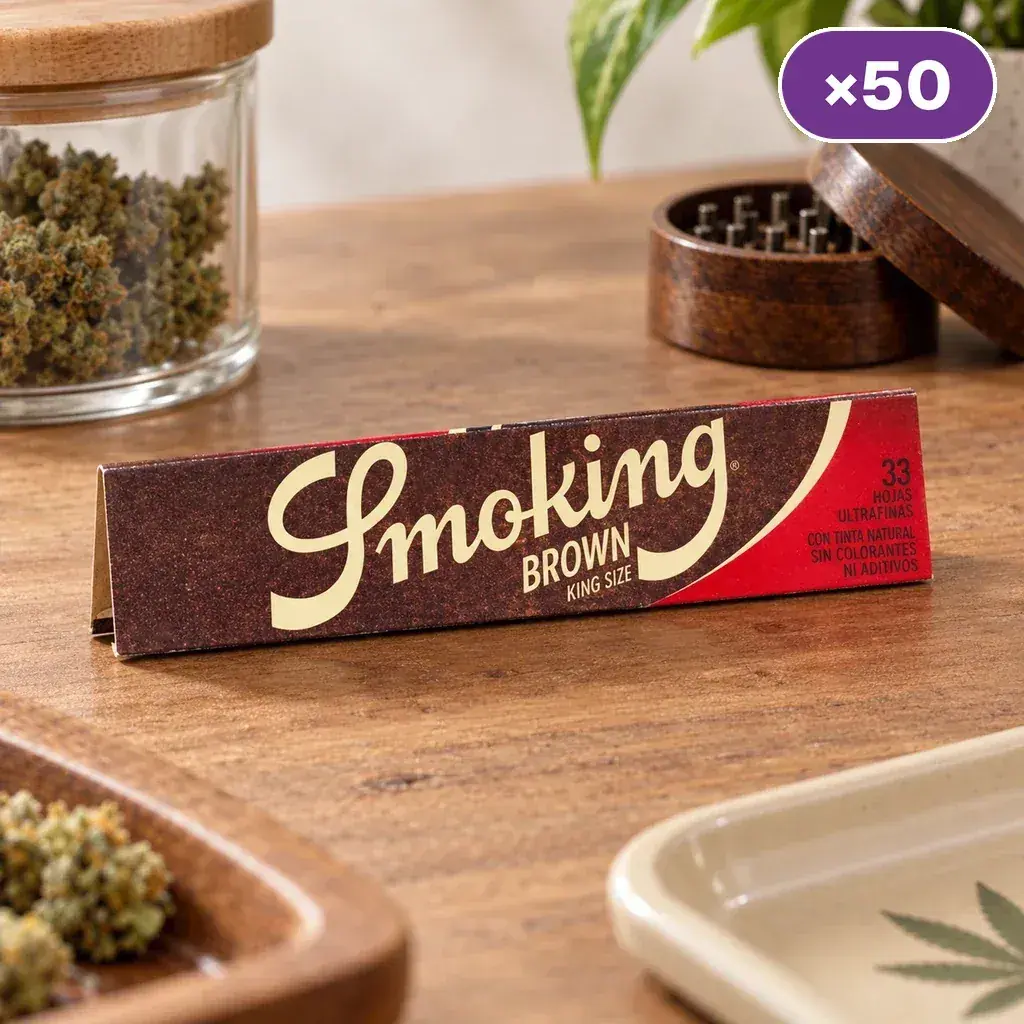 Librillo Smoking Brown King Size sobre una mesa de madera, con un tarro de cogollos y un grinder al fondo y un distintivo «×50».