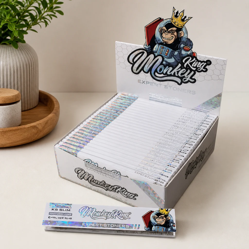 Expositor de papeles Monkey King Expert Stoners KS Slim con acabado holográfico y un mono coronado, junto a un librillo sobre la mesa.