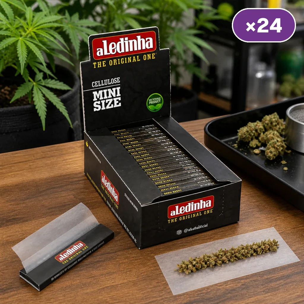 Expositor Aledinha Mini Size con distintivo ×24, un librillo abierto y una hoja translúcida con hierba desmenuzada sobre una mesa.