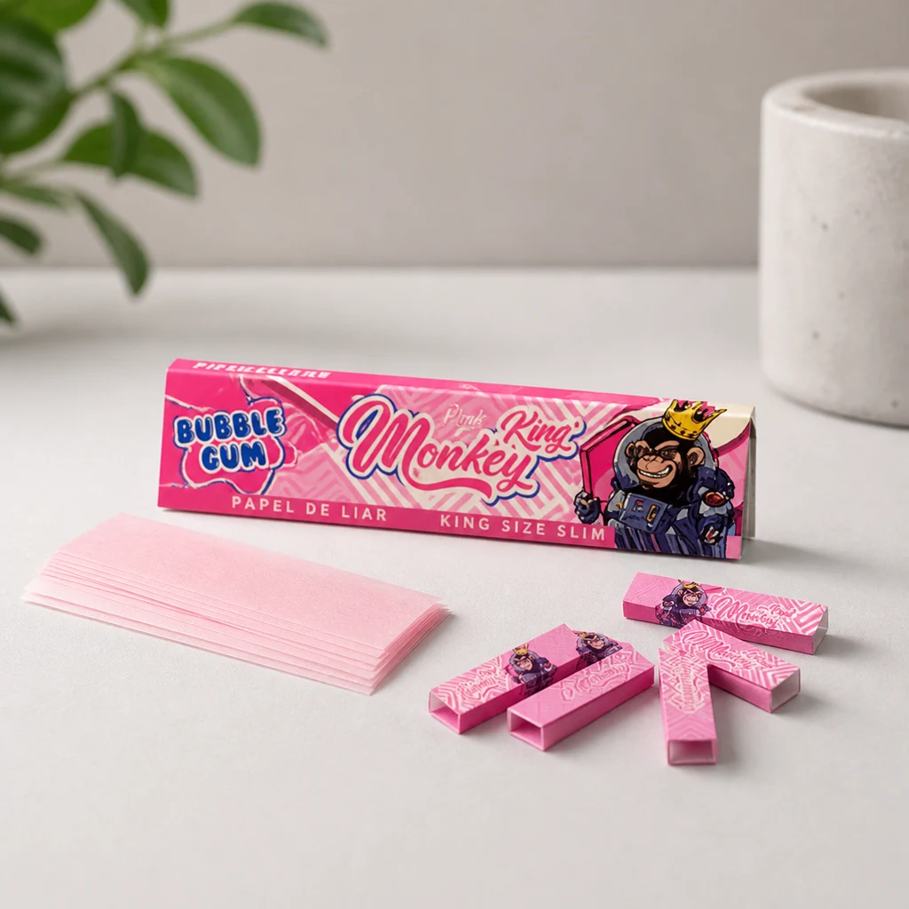 Estuche rosa Monkey King Bubble Gum con hojas rosas de papel de liar y varias boquillas rectangulares sobre una mesa clara.