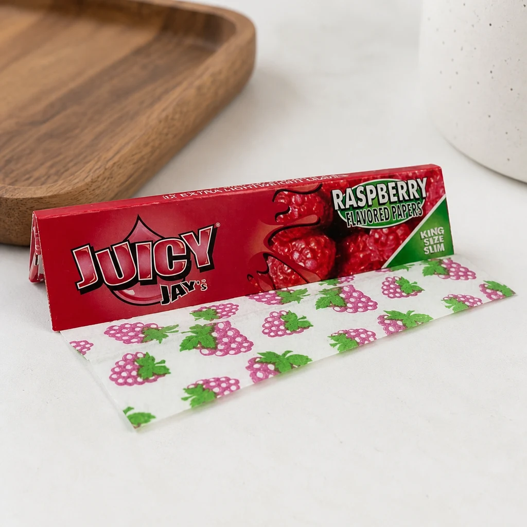 Librillo rojo Juicy Jay's King Size de frambuesa con una hoja extendida decorada con frambuesas sobre una superficie clara.