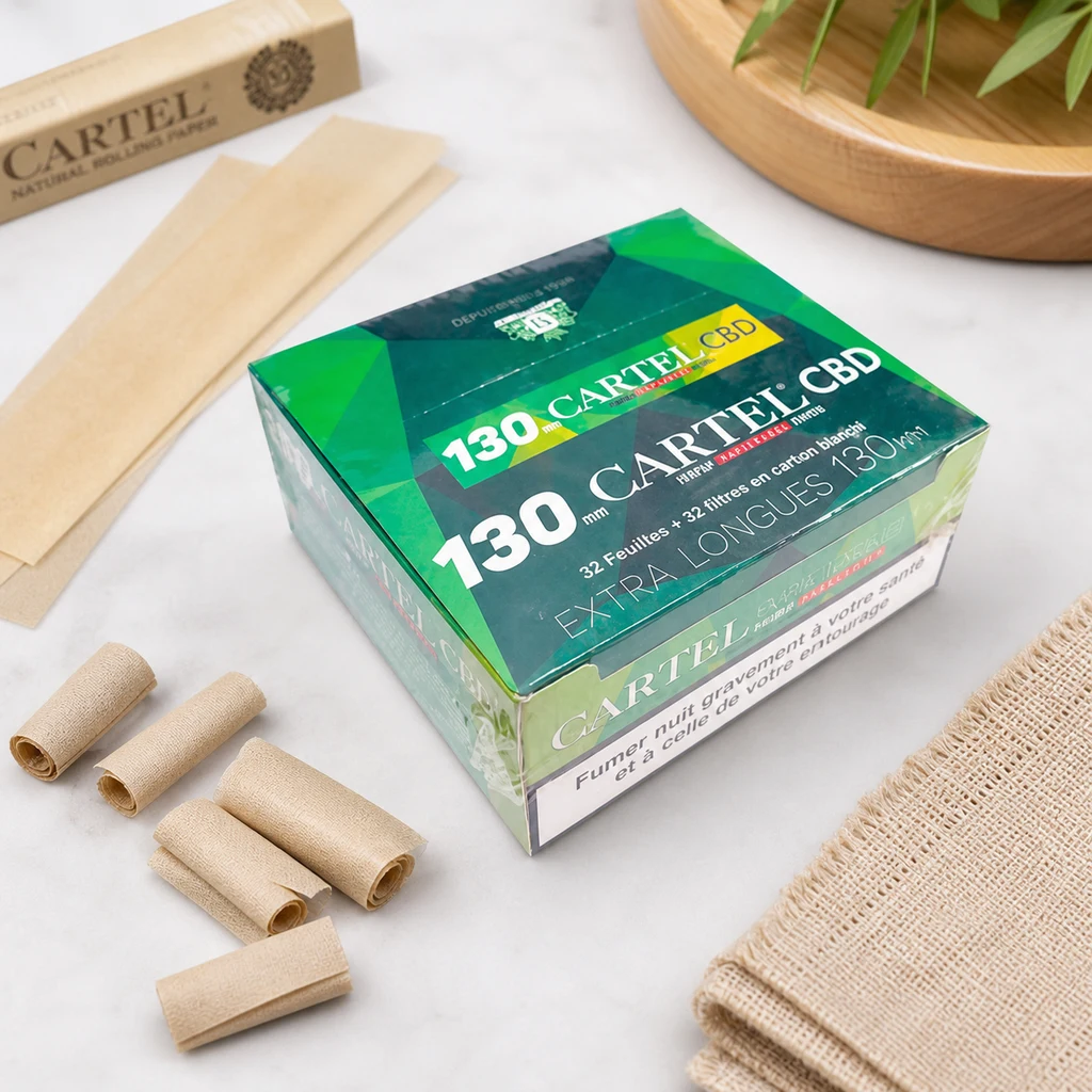 Caja verde de papel de liar Cartel de 130 mm y tips CBD, rodeada de papeles y boquillas enrolladas sobre una superficie clara.