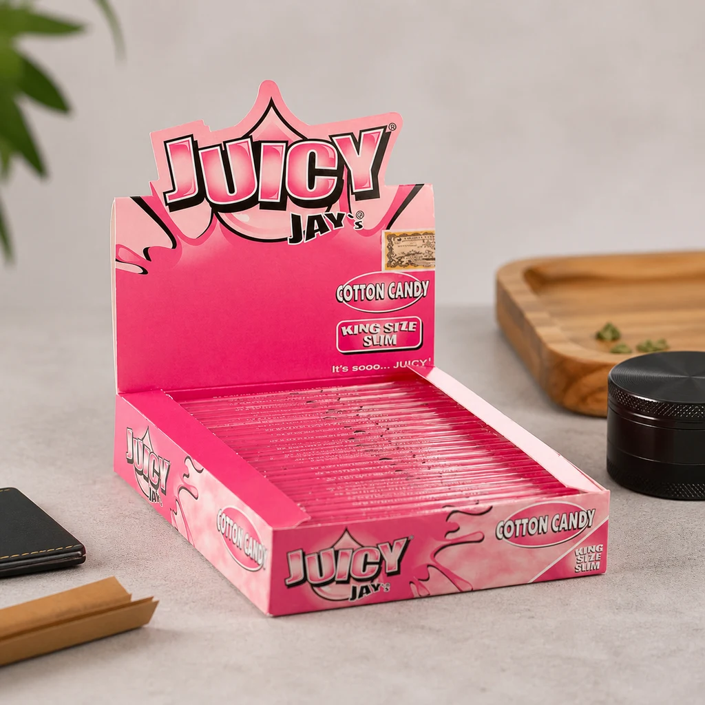 Expositor rosa abierto de papeles Juicy Jay's Cotton Candy King Size Slim, con varias unidades junto a un grinder negro y una bandeja.