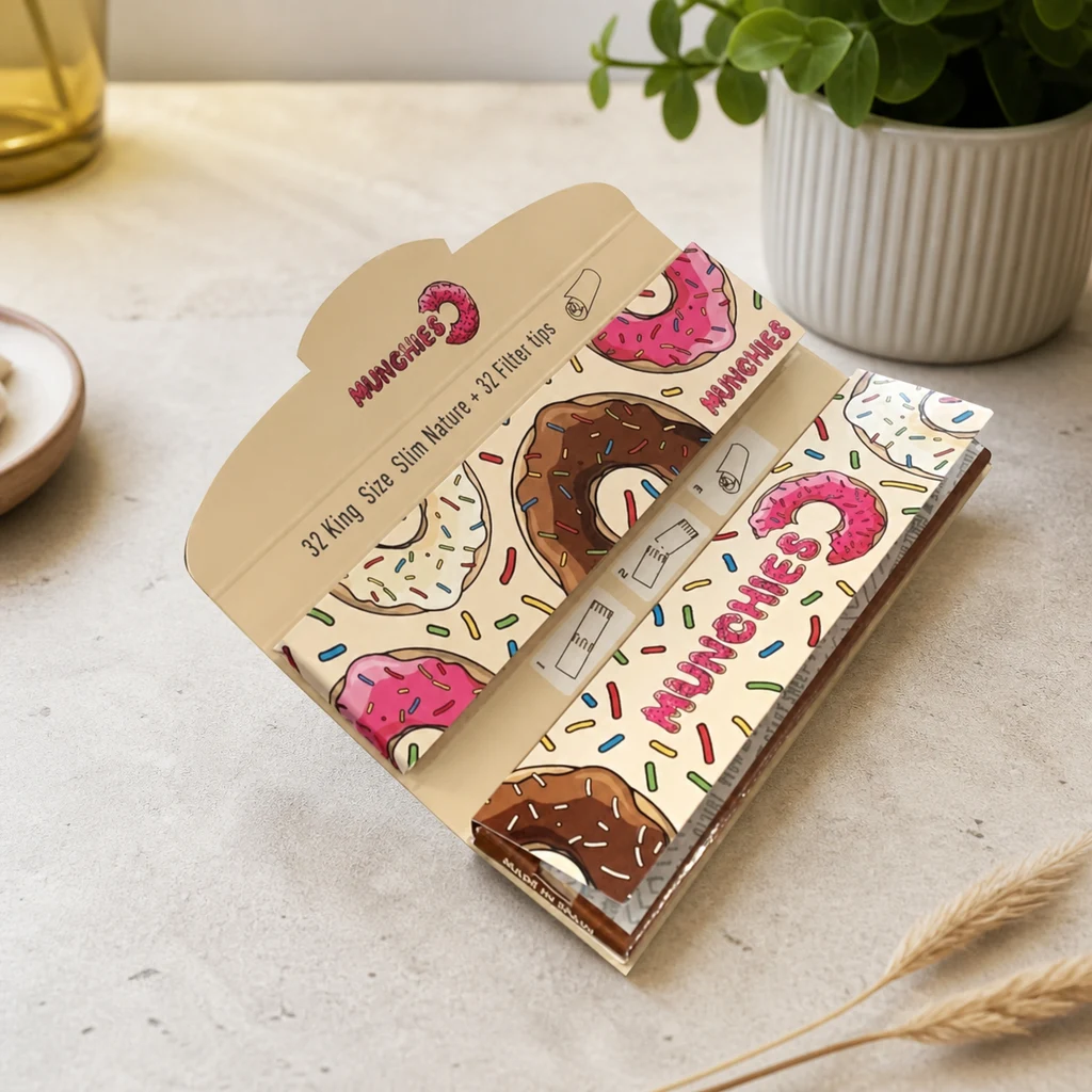 Estuche abierto de papel de liar Munchies King Size Slim con filtros, decorado con rosquillas y virutas de colores sobre una mesa clara.