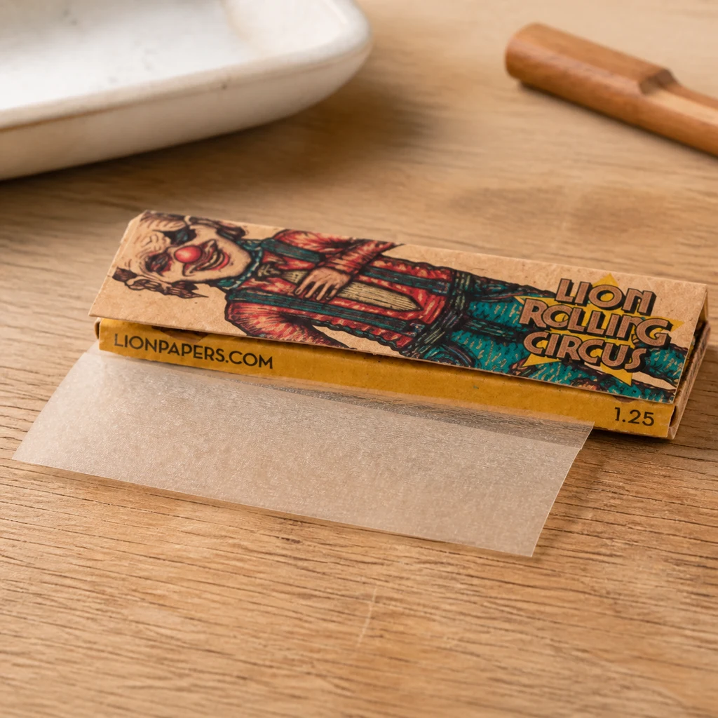 Librillo de papel Lion Rolling Circus Natural con un payaso ilustrado y una hoja translúcida extendida sobre una mesa de madera.