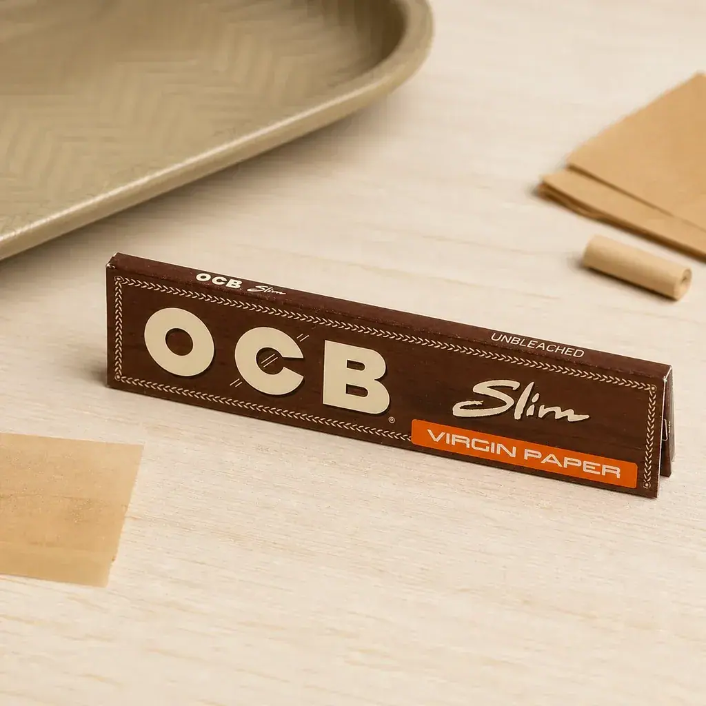 Librito marrón de papel OCB Slim Virgin sobre una mesa clara, junto a hojas de papel y una bandeja parcialmente visible. Librito marrón de papel OCB Slim Virgin sobre una mesa clara, junto a hojas de papel y una bandeja parcialmente visible.