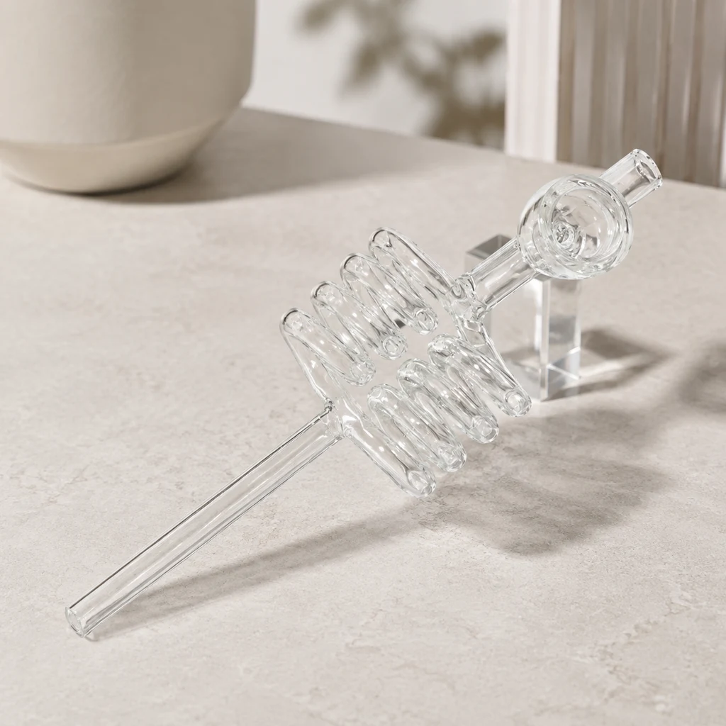 Pipa de cristal transparente con doble espiral central, tubo largo y cazoleta redonda, colocada en diagonal sobre una superficie beige.