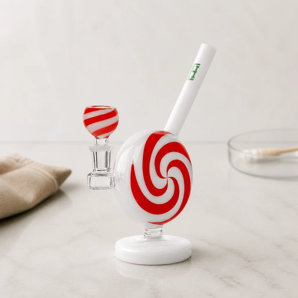 Bong Jollypop de Hemper con cuerpo circular de espiral roja y blanca, tubo inclinado y cazoleta lateral sobre una encimera.