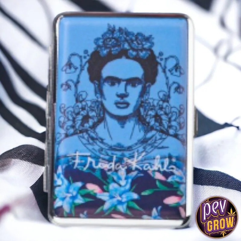 Pitillera Frida Collection con borde metálico y retrato azul de Frida Kahlo entre flores, sobre tela blanca y negra.
