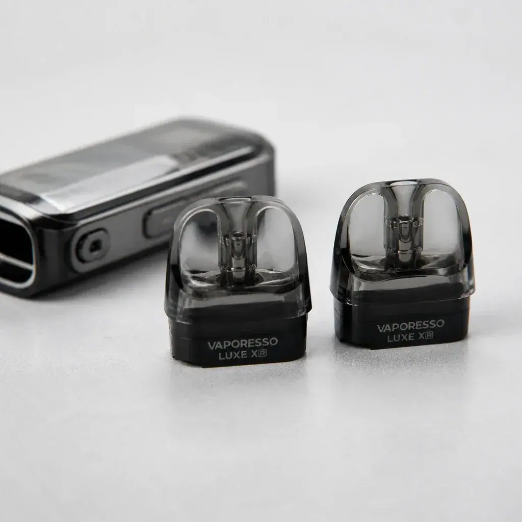 Pods Vaporesso Luxe XR con depósito transparente y base negra, en primer plano junto a un dispositivo desenfocado.