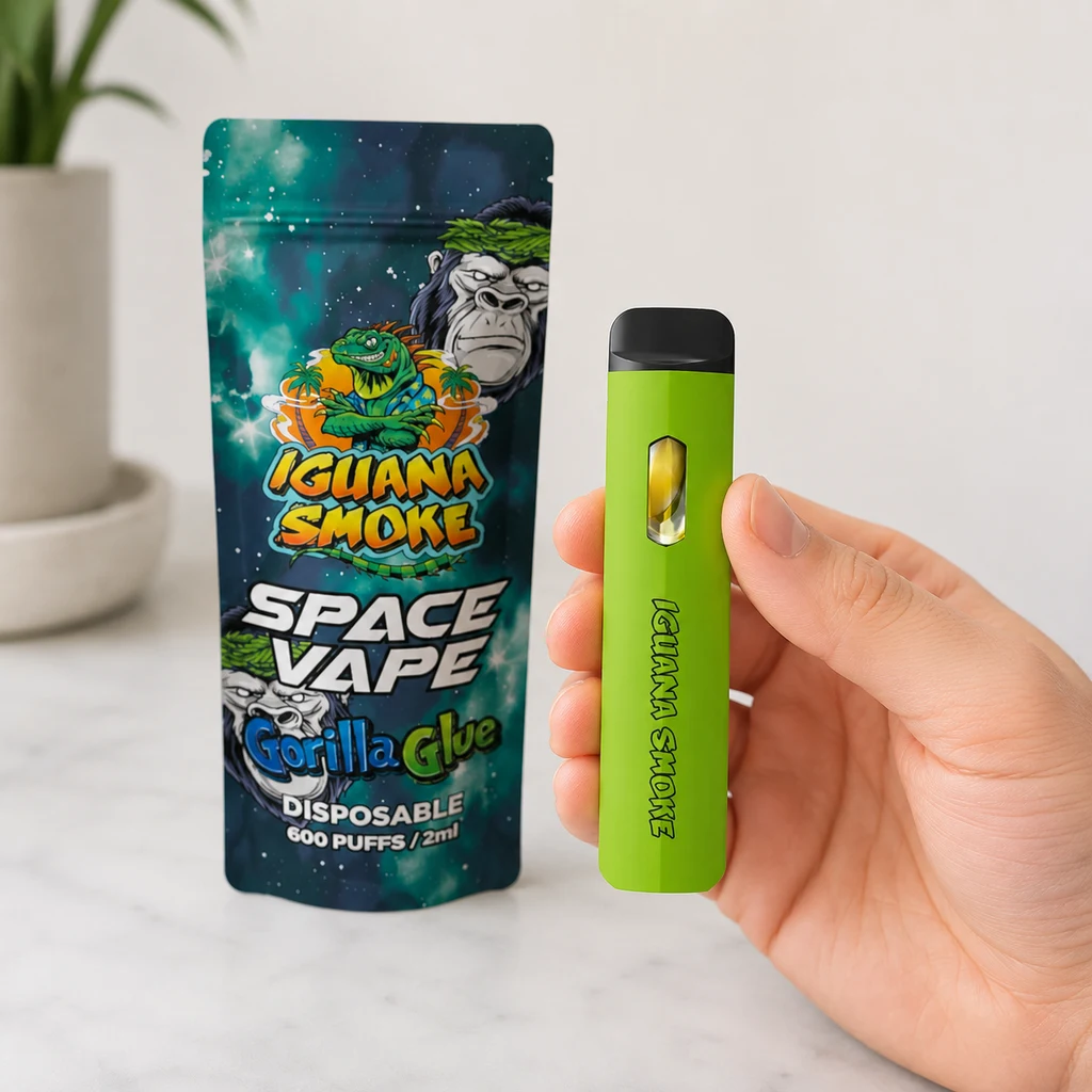 Una mano sostiene un vapeador verde con boquilla negra junto a una bolsa Iguana Smoke Space Vape Gorilla Glue sobre una mesa clara.