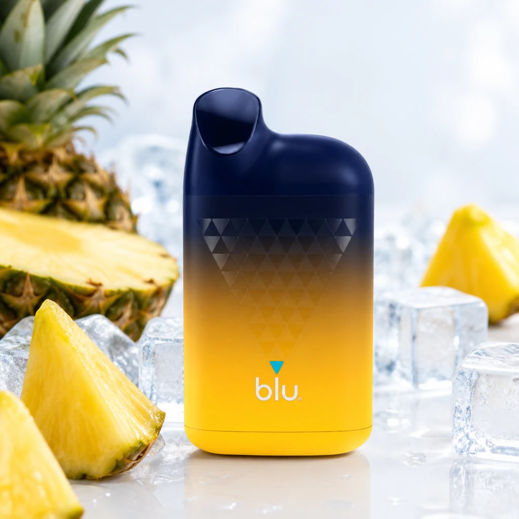 Pod Blu Box Pineapple Ice con cuerpo degradado de azul oscuro a amarillo y boquilla integrada, entre trozos de piña y cubitos de hielo.
